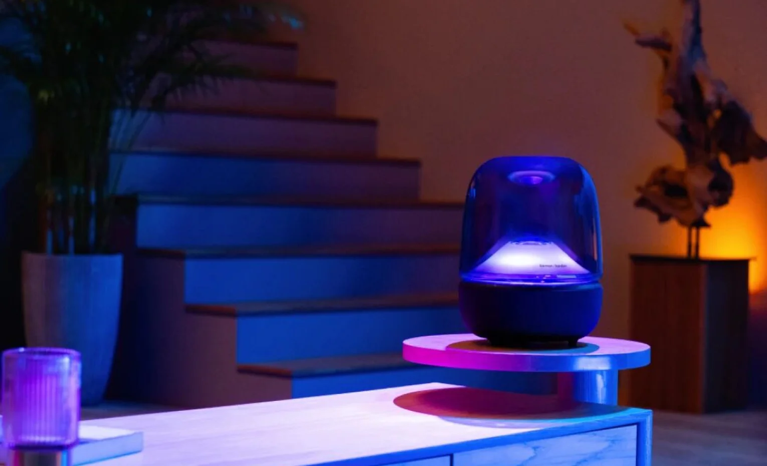 اسپیکر هارمن کاردن Aura Studio 5 روی میز کنار راهپله در فضای آبی و بنفش اسپیکر هارمن کاردن Aura Studio 5 روی میز کنار راهپله در فضای آبی و بنفش